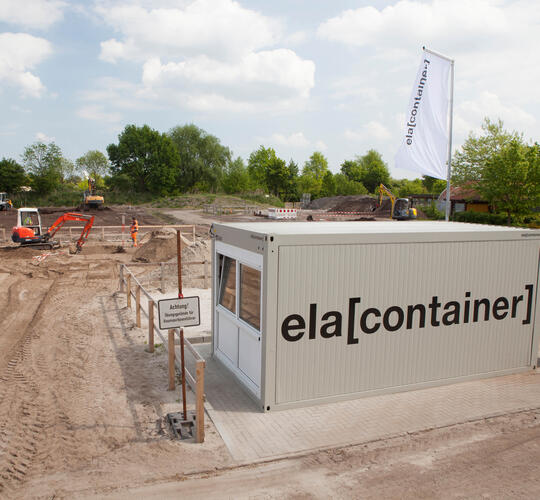 Außenansicht einzelner Baucontainer auf Baustelle mit Logo von ELA Container