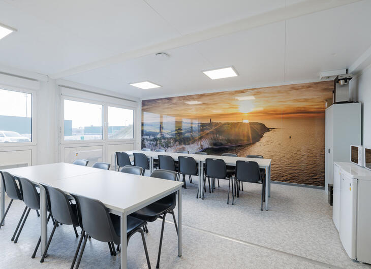 Aufenthtalscontainer mit verschiedenen Sitzbereichen und grafischer Hinterwand in Küstenoptik