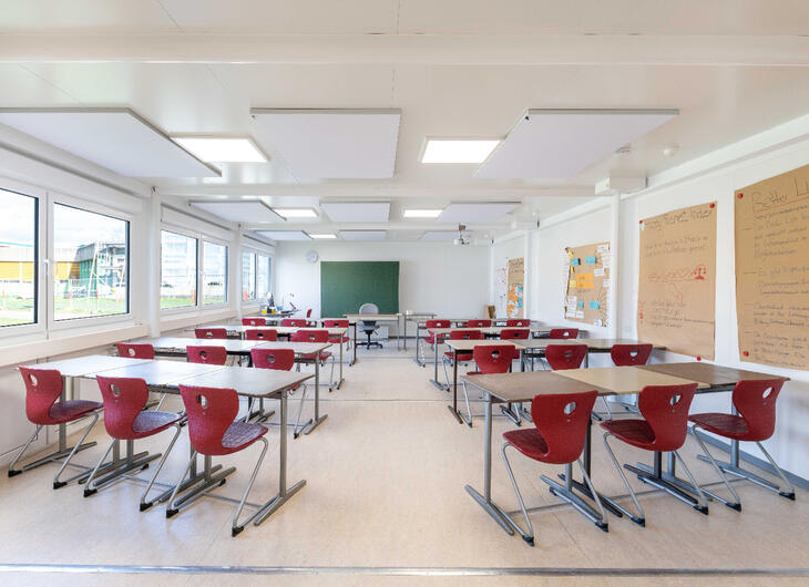 Innenansicht Schulcontainer mit Tischen, Stühlen und einer großen Tafel