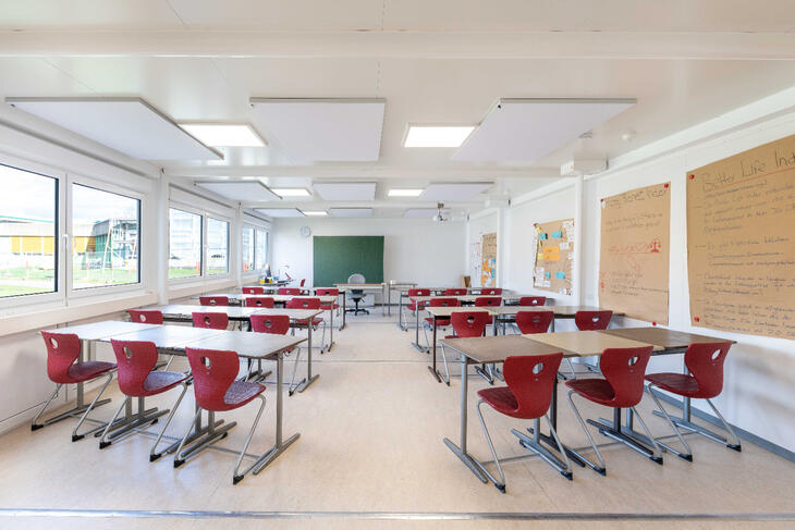 Innenansicht Schulcontainer mit Tischen, Stühlen und einer großen Tafel